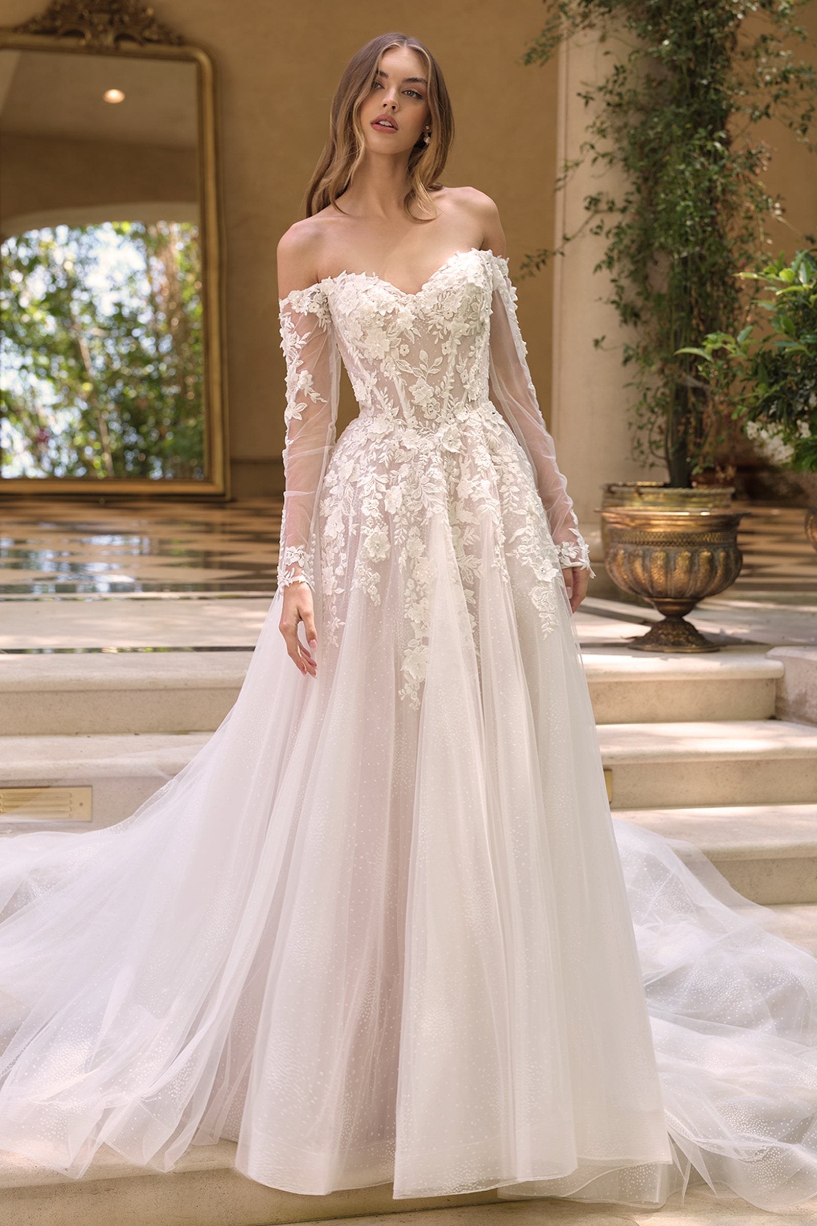 Andrea & Leo WL067 is a women’s wedding dress for wedding, formal events. Source details list a Ball gown silhouette. Design details include Off-the-shoulder sweetheart neckline with sheer illusion sleeves & 3D floral lace appliqué. Fabric/material details: Glittered tulle skirt layered beneath lace-appliqued bodice. Fit detail: Structured corset-style bodice with boning for shape and support. Colors listed: off white/nude. Use the product options for exact color and size selection.